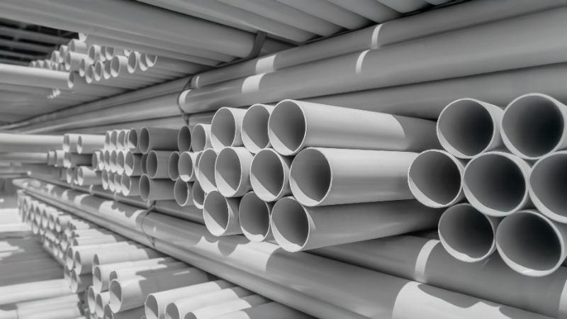 Mga patong ng kulay-abong PVC pipe na iba-iba ang diameter, nakaimbak sa rack sa bodega, nakaharap ang dulo