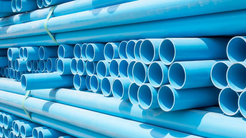 Mga bungkos ng light blue na plastic pipe na nakatali at nakasalansan, kita ang bukas na dulo