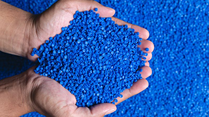 Manos ahuecadas sostienen un montón de granza de plástico azul sobre una capa de la misma granza