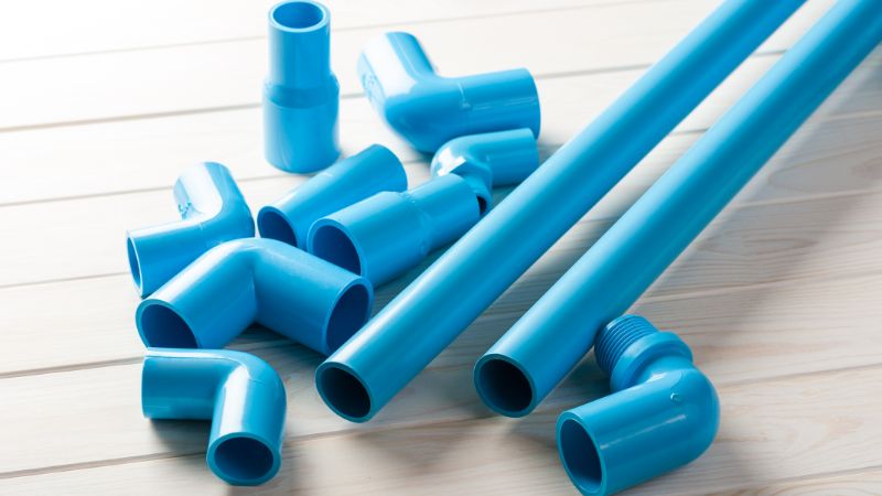 Blue plastic pipes with elbow, tee, coupling and threaded fittings laid out on a white wooden surface