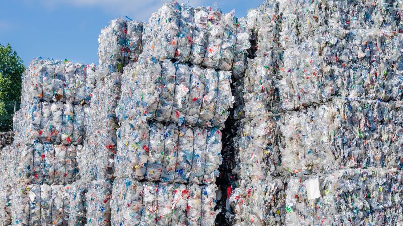 Timbunan tinggi bandela mampat botol plastik terpakai di luar di bawah langit biru