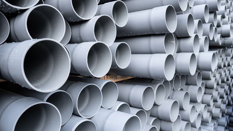 Malapitang kuha ng nakasalansang kulay-abong plastic pipe na may bell end, kita ang kapal ng pader ng tubo