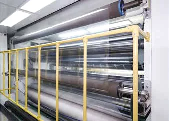 Precision rollers processing transparent film behind a yellow safety rail
