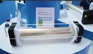 Серебристый цилиндрический рулон между чёрными торцевыми опорами на выставочном стенде